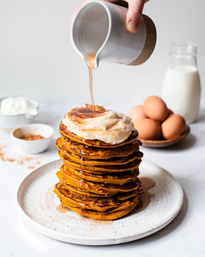 a stack of pumpkin pancakes topped with whipped cream, cinnamon, and maple syrup