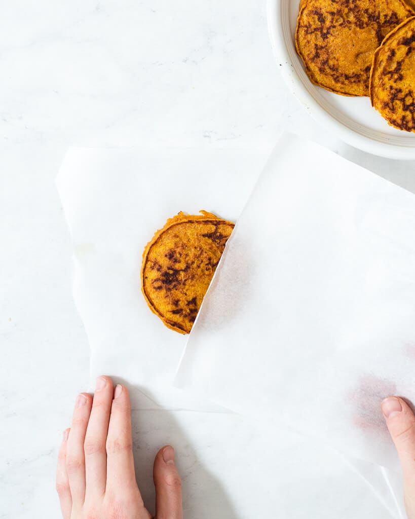 a person freezing pumpkin pancakes in between sheets of parchment paper