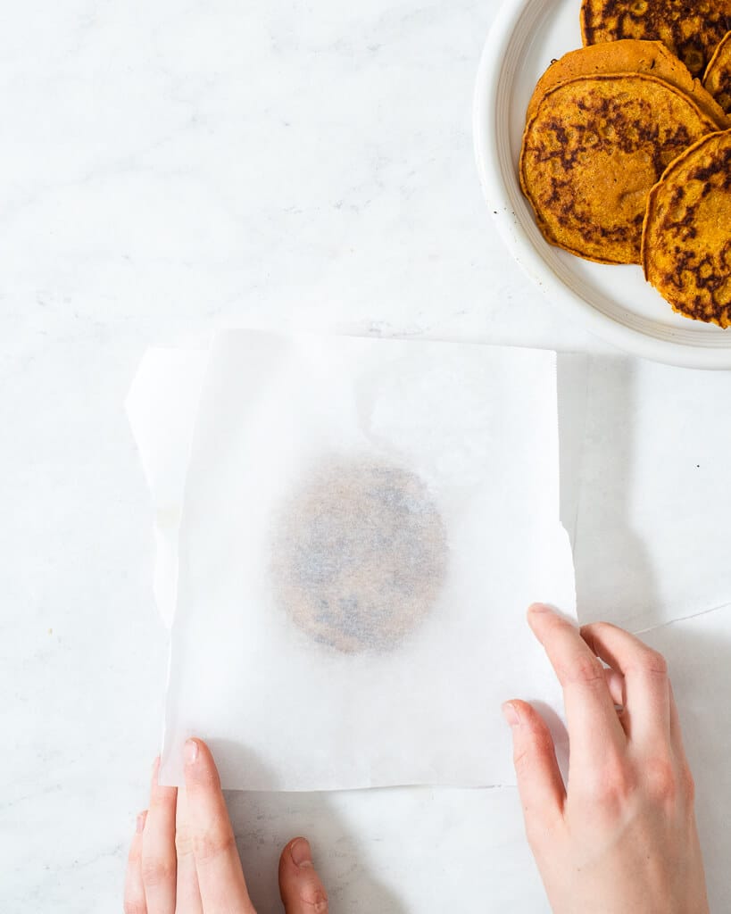 a person freezing pumpkin pancakes in between sheets of parchment paper