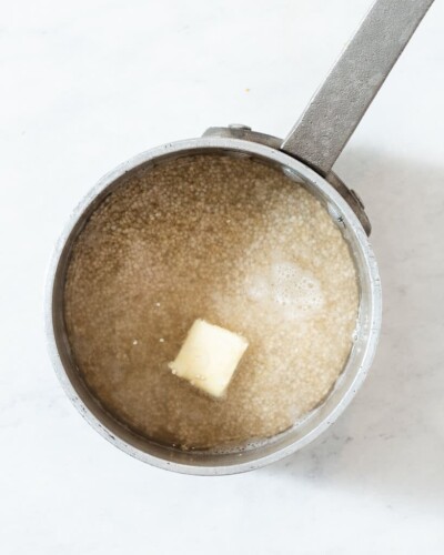 a stainless steel pot of dry quinoa, water, and butter