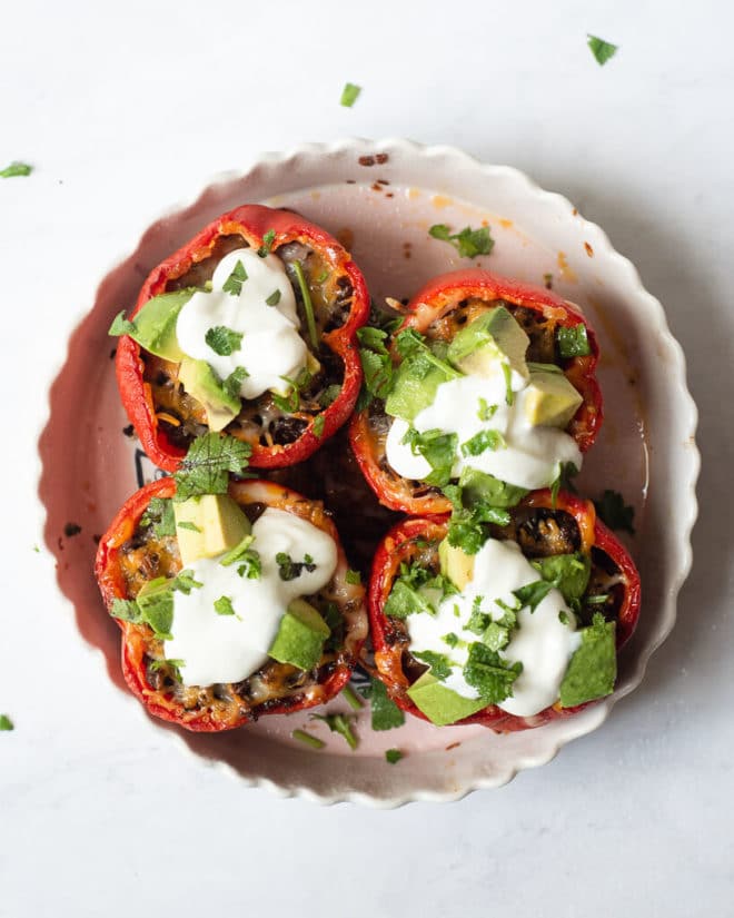 a baking dish of 4 tex mex stuffed peppers garnished with sour cream, avocado, and cilantro