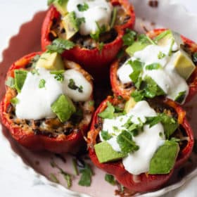 a baking dish of 4 tex mex stuffed peppers garnished with sour cream, avocado, and cilantro