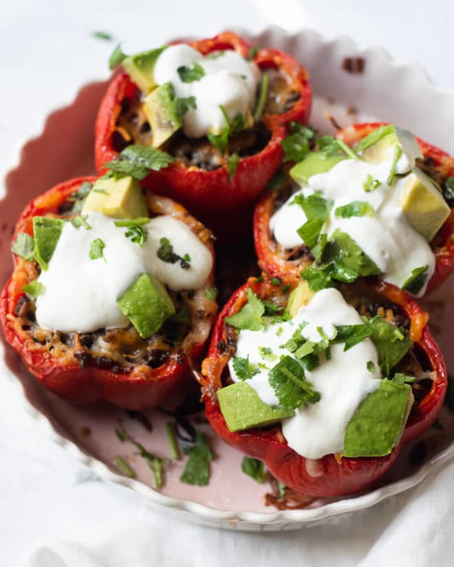 a baking dish of 4 tex mex stuffed peppers garnished with sour cream, avocado, and cilantro