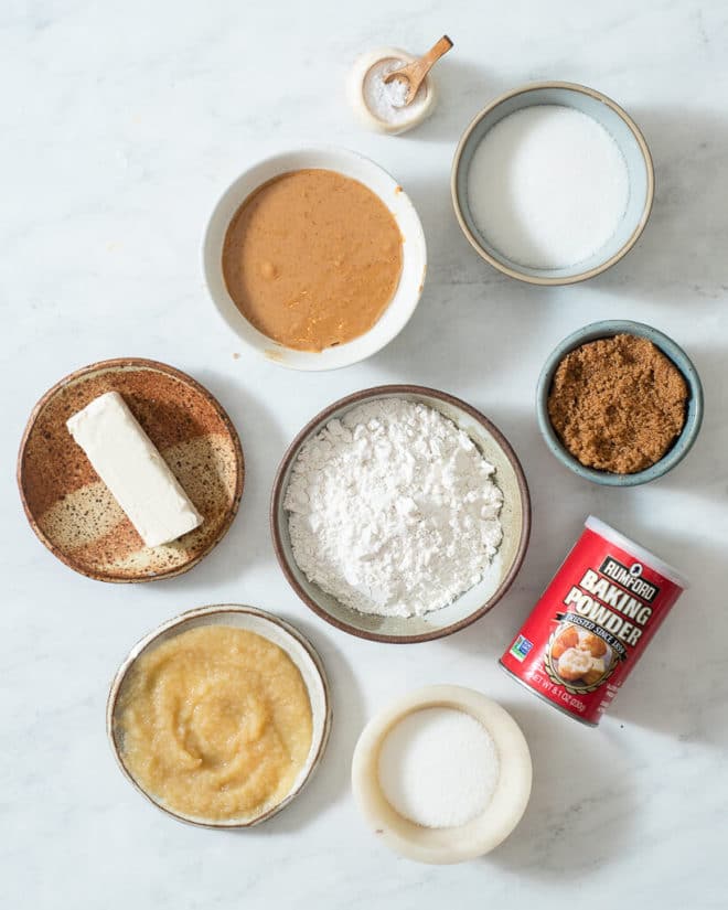 ingredients for vegan pb cookies in different sized bowls on a marble surface