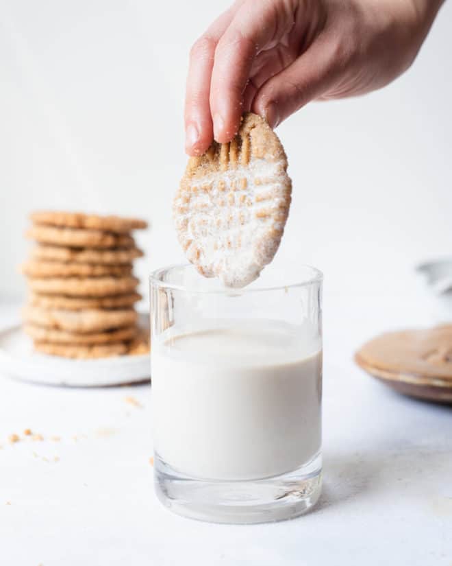 a person dipping a vegan pb cookie into a glass of milk