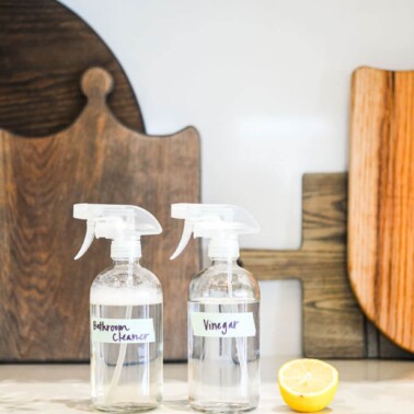 spray bottles of vinegar and bathroom cleaner next to a halved lemon on a counter