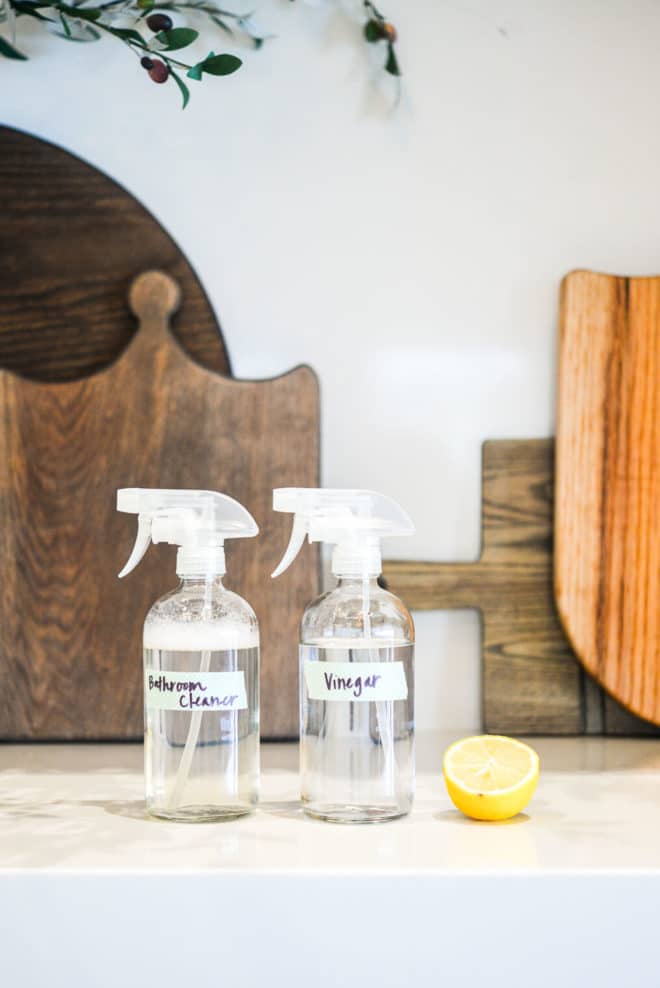 spray bottles of vinegar and bathroom cleaner next to a halved lemon on a counter