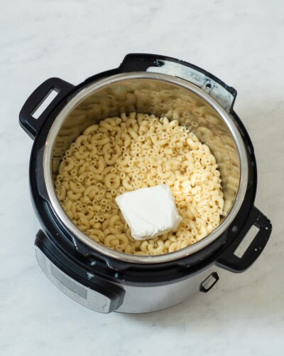 cooked macaroni noodles in an instant pot with a block of cream cheese sitting on top