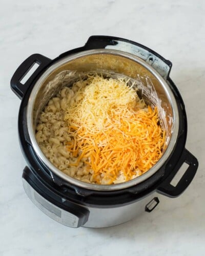 an instant pot with cooked macaroni in it and shredded cheese on top