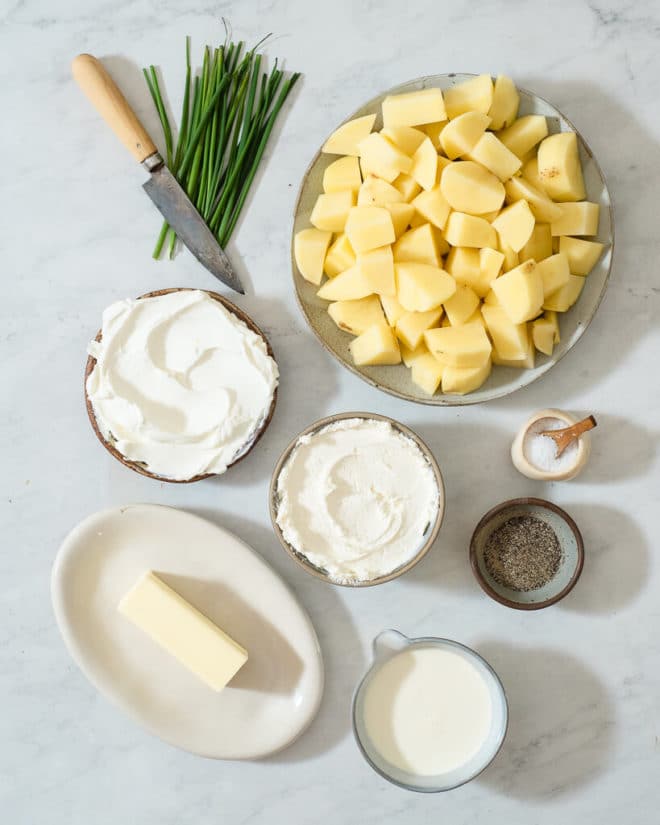 all of the ingredients for creamy mashed potatoes in different sized bowls on a marble surface