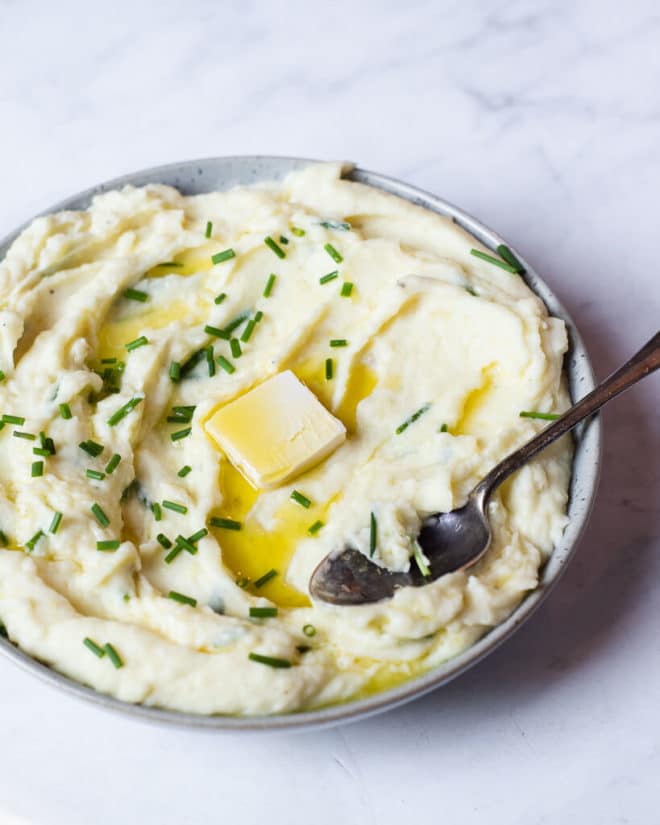 a bowl of creamy mashed potatoes garnished with chives and a pat of butter