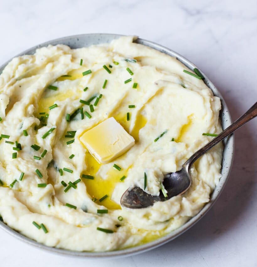 a bowl of creamy mashed potatoes garnished with chives and a pat of butter