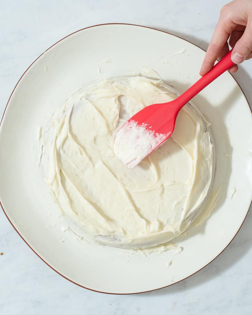 a person using a spatula to frost a red velvet cake