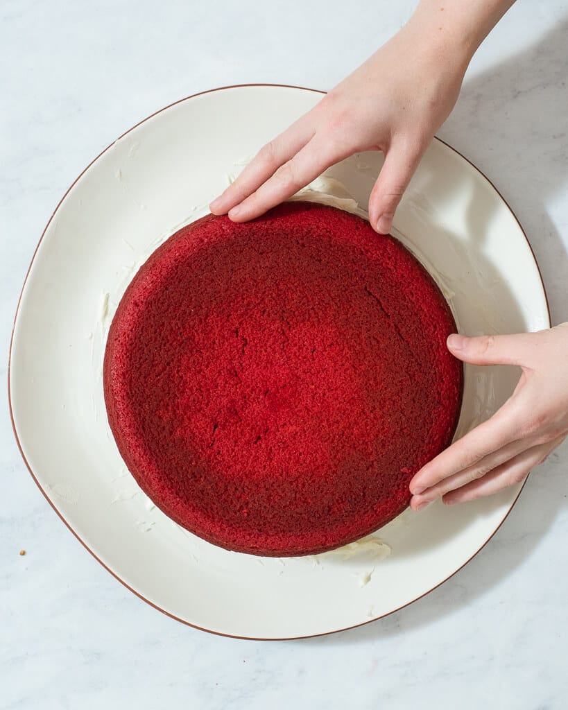 a person stacking two round red velvet cakes on top of each other