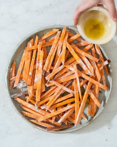 a person drizzling olive oil over a plate of sweet potato fries