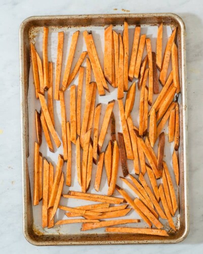 a stainless baking sheet with uncooked sweet potato fries on it