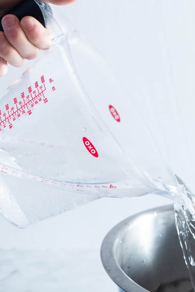 a person pouring the water out of a measuring cup