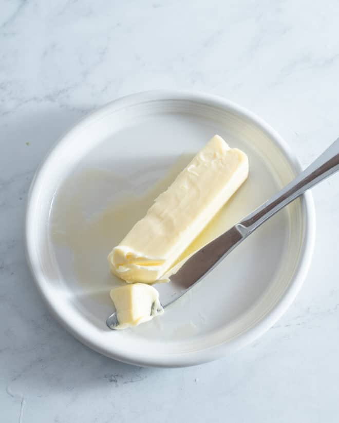 a stick of softened butter on a small white plate with a butter knife next to it