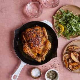 roasted chicken next to arugula salad and roasted potato wedges