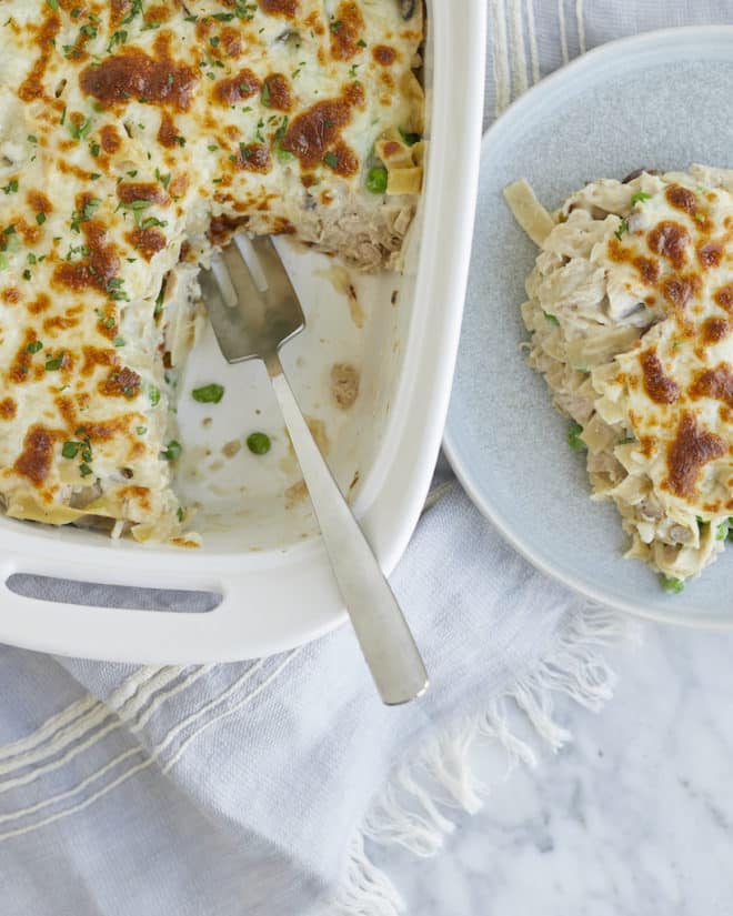 a serving of tuna noodle casserole on a plate next to a casserole dish of tuna noodle casserole