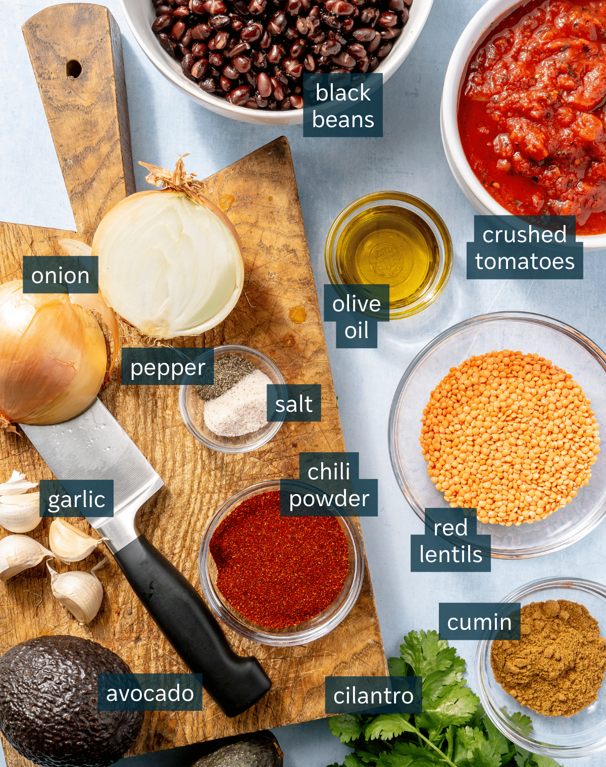 Ingredients for vegetarian chili sit on a chopping block and in a variety of bowls on a blue countertop.