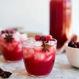 two cranberry margaritas sitting in front of a large pitcher of cranberry margaritas