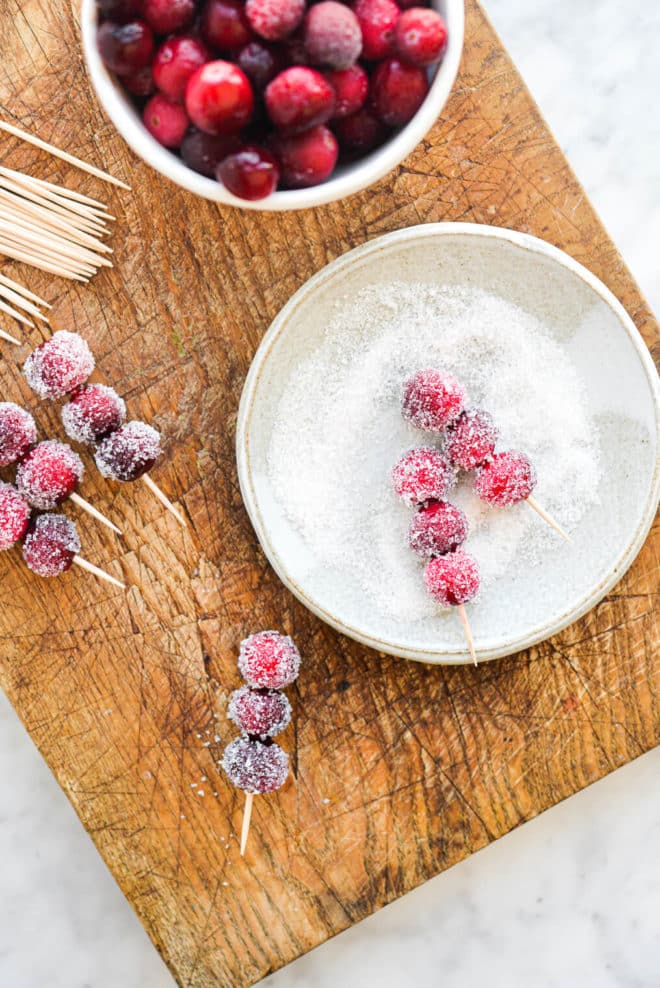 skewered cranberries being rolled in a plate of sugar