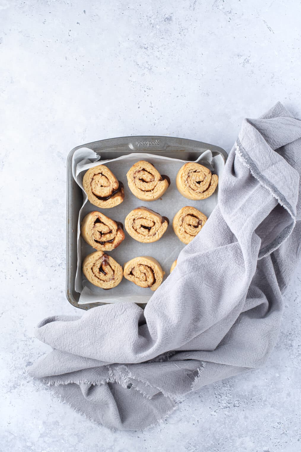 a pan of keto cinnamon rolls with a kitchen towel over them before rising to go into the oven