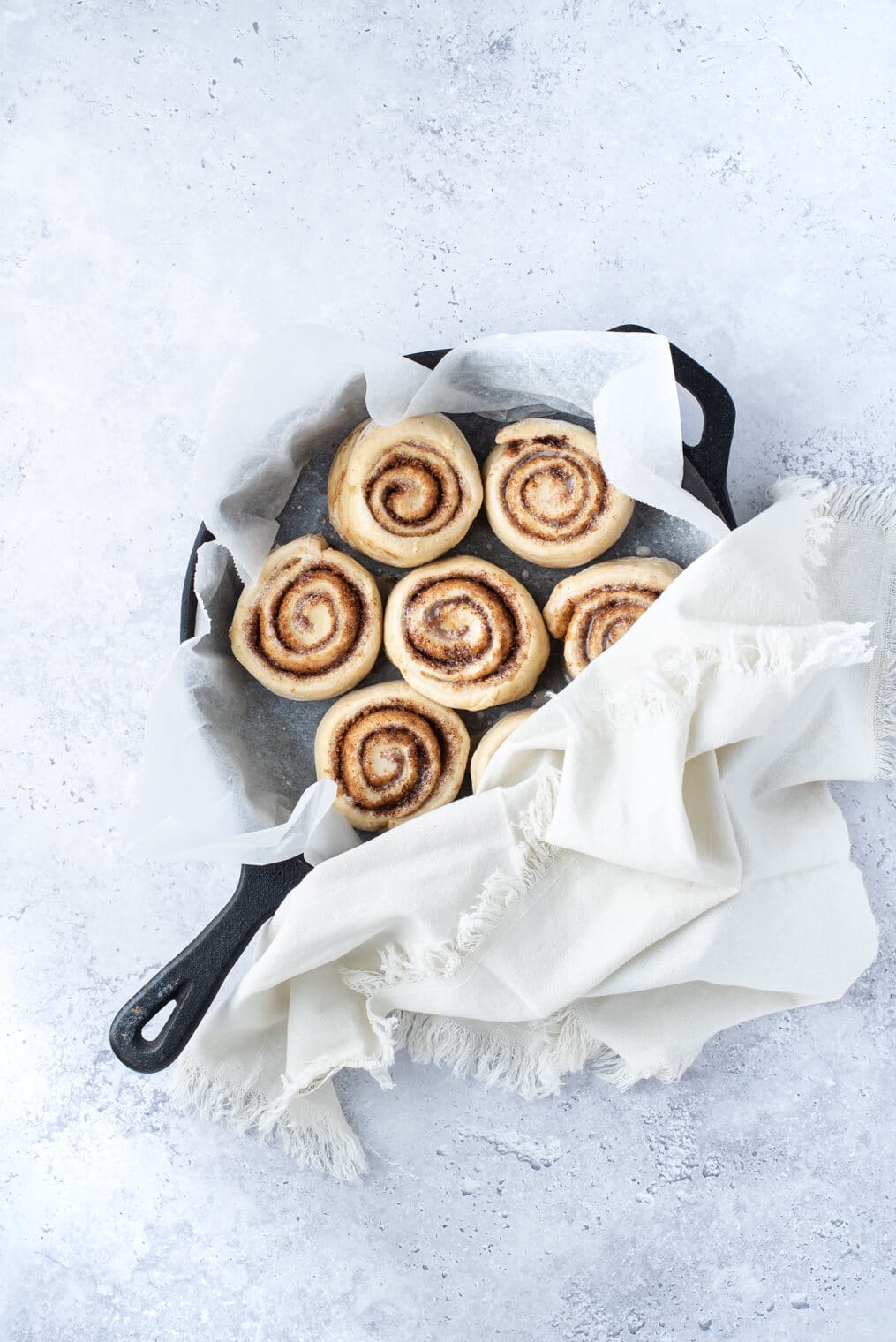 a pan of vegan cinnamon rolls covered with a kitchen towel before rising for a second time