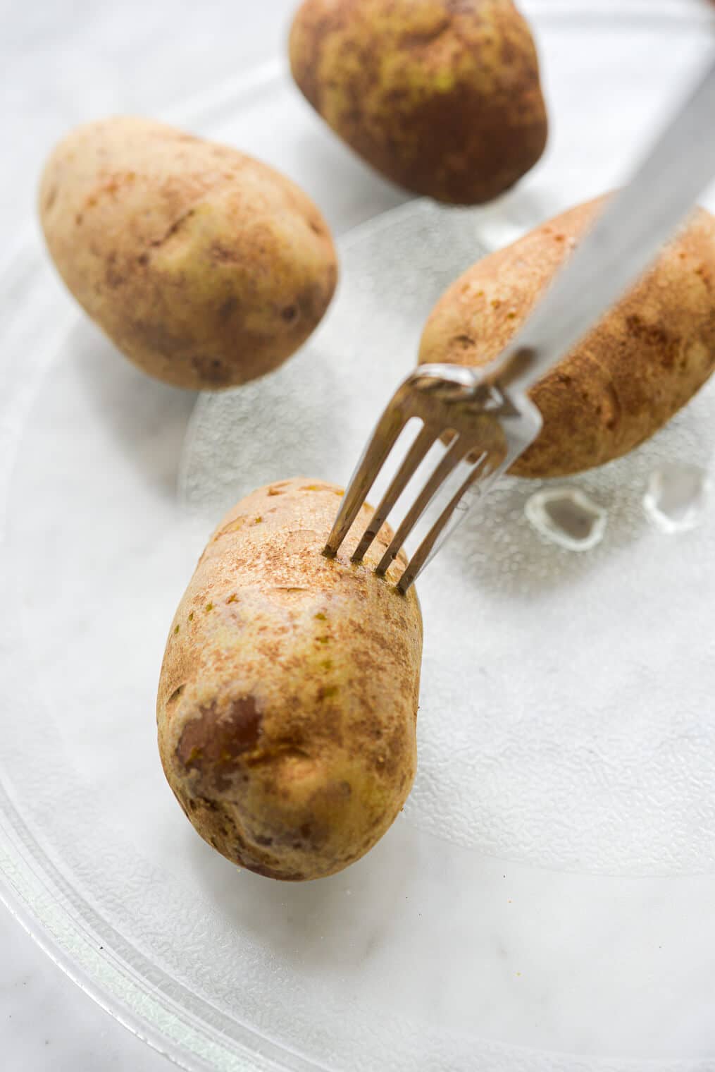a person using a fork to poke holes in potatoes before microwaving them
