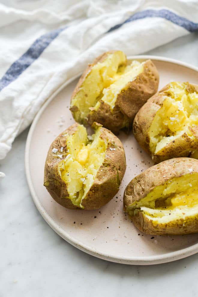 finished microwaved baked potatoes split open and loaded with butter, salt, and pepper