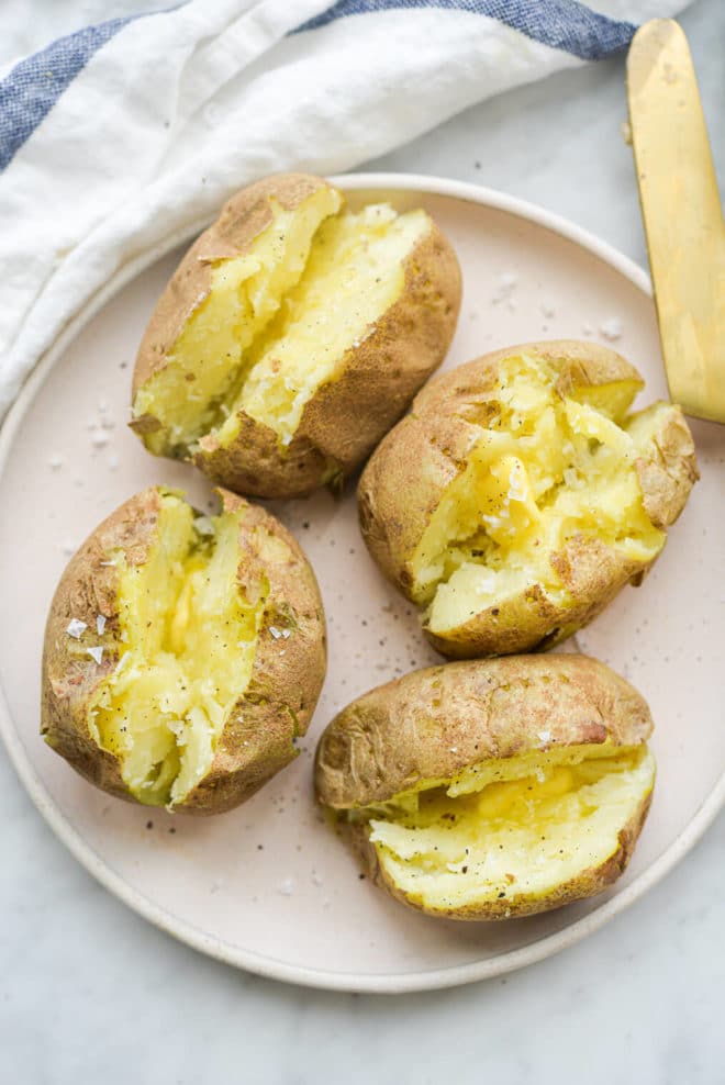 finished microwaved baked potatoes split open and loaded with butter, salt, and pepper