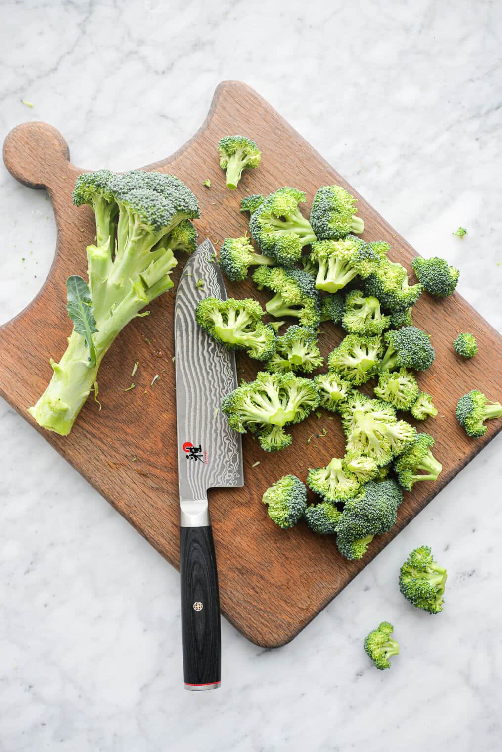 a cutting board of chopped broccoli florets next to a large knife