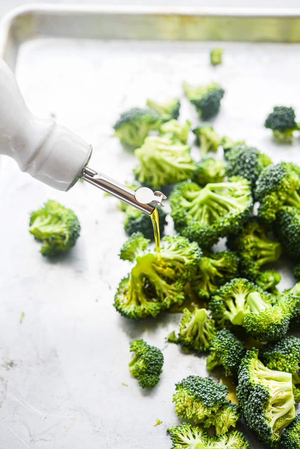a sheet pan of broccoli florets being drizzled with olive oil