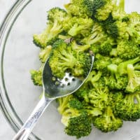 a glass bowl of steamed broccoli with a spoonful of it being held over the bowl