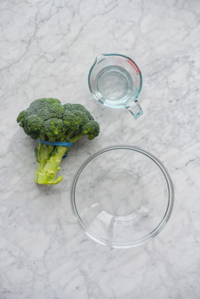 the ingredients needed for steamed broccoli on a marble surface