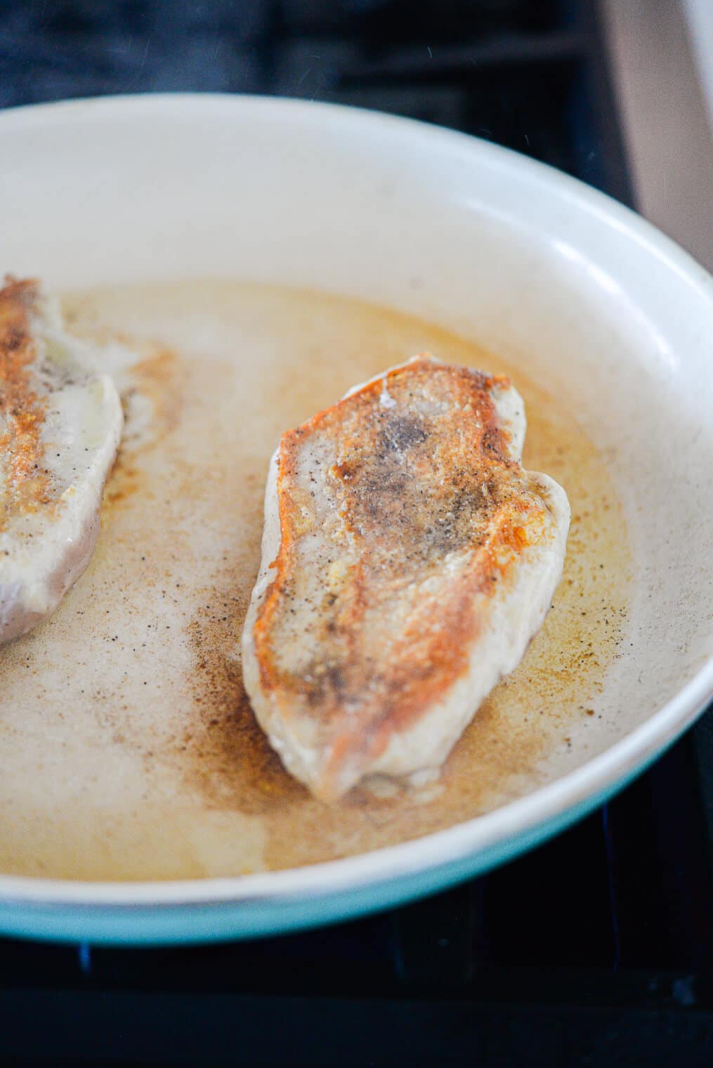 chicken breasts searing in a pan with olive oil