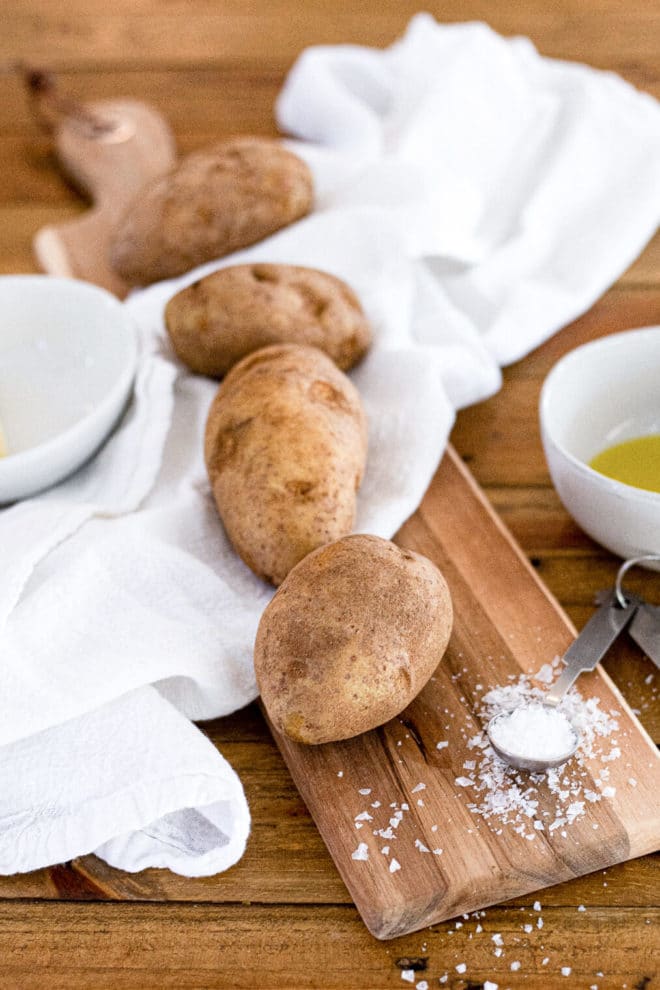 4 potatoes next to olive oil and a teaspoon of salt