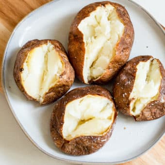 4 air fryer baked potatoes split open with butter in them