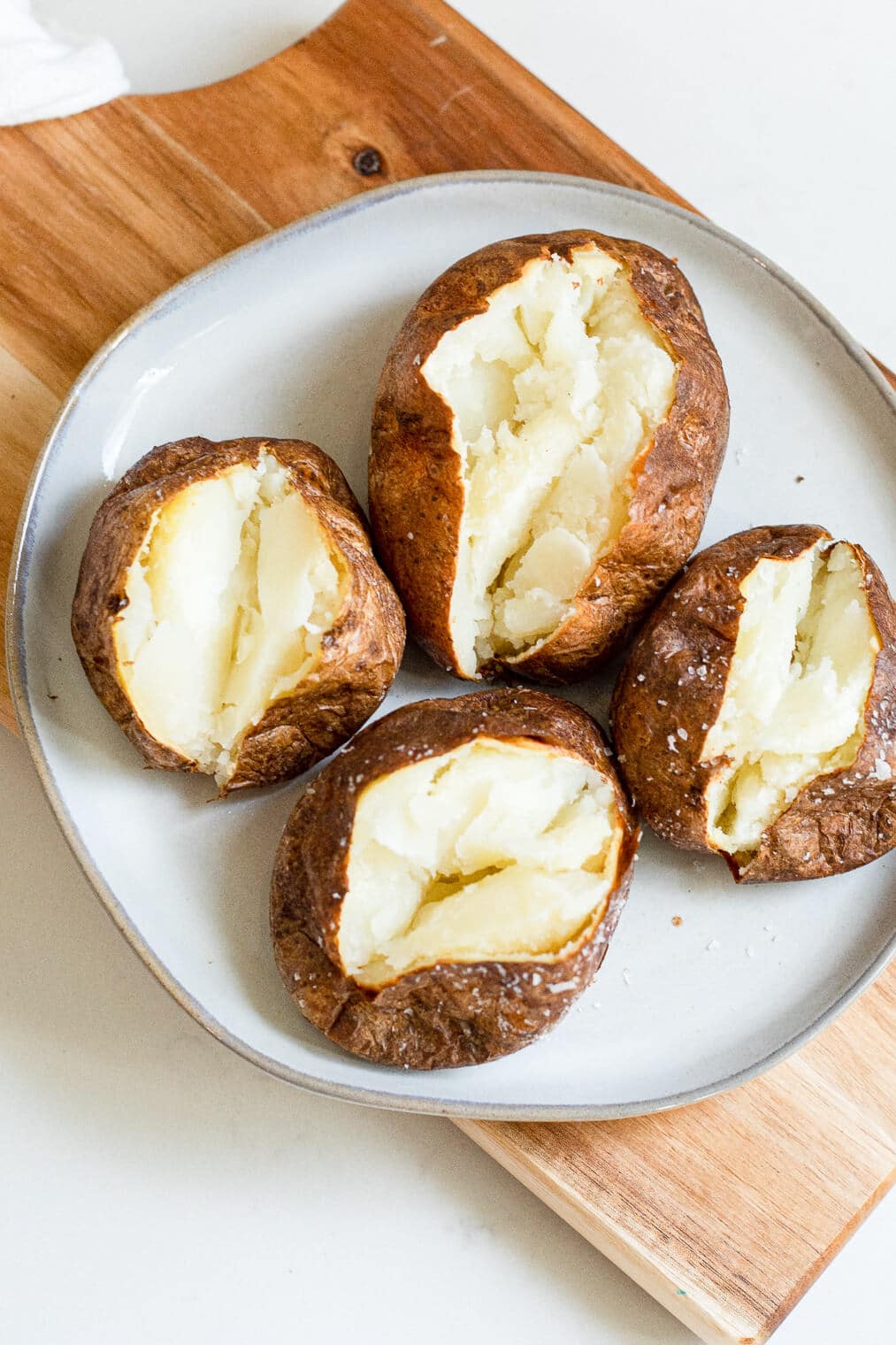 4 air fryer baked potatoes split open with butter in them