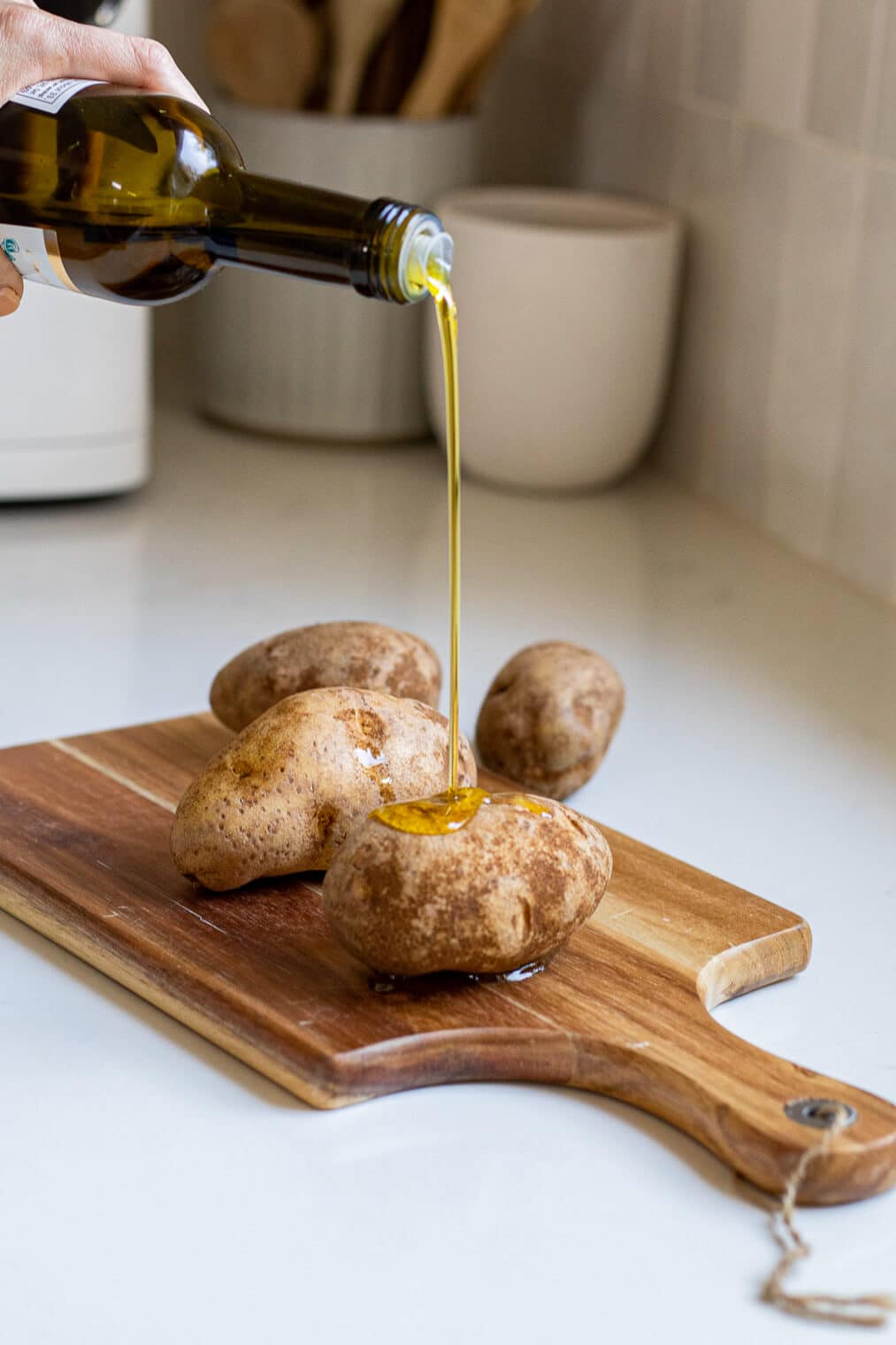 a person pouring olive oil over a potato on a cutting board