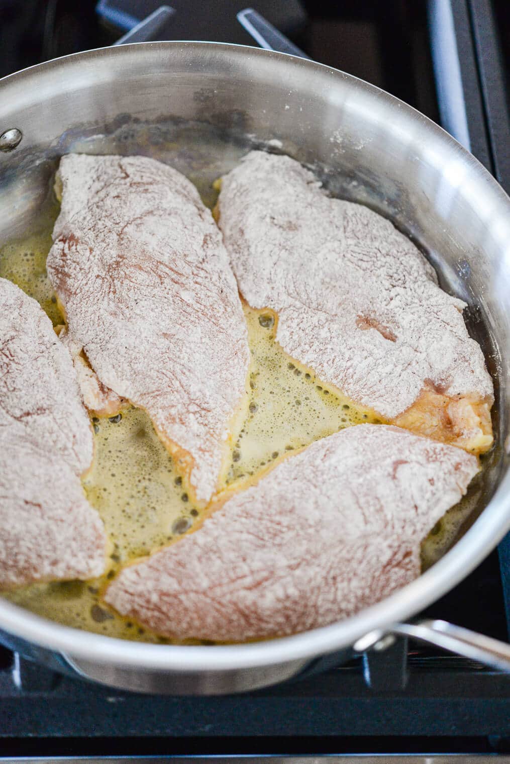 flour coated chicken breasts searing in a skillet of butter