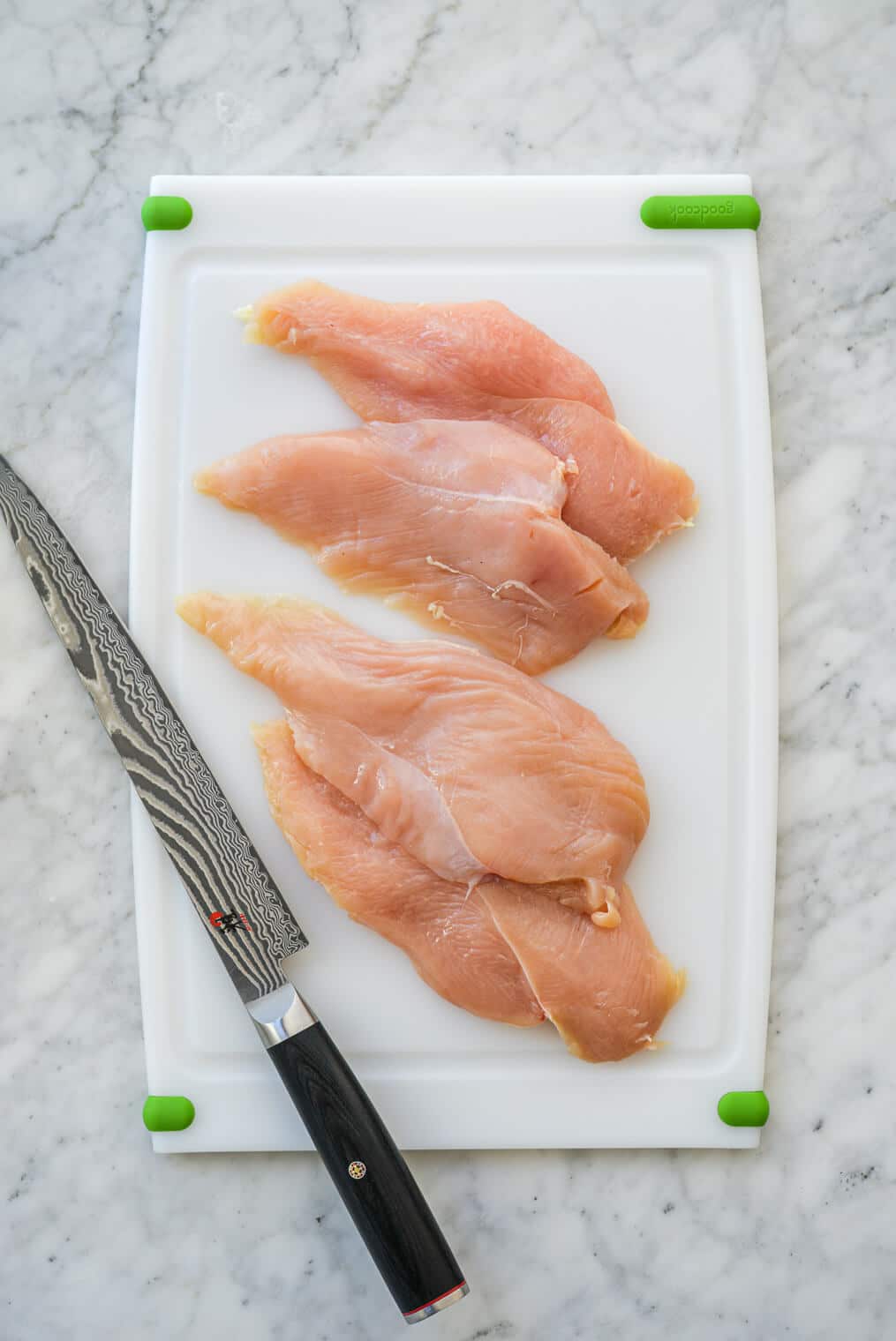 halved chicken breasts on a cutting board next to a large knife