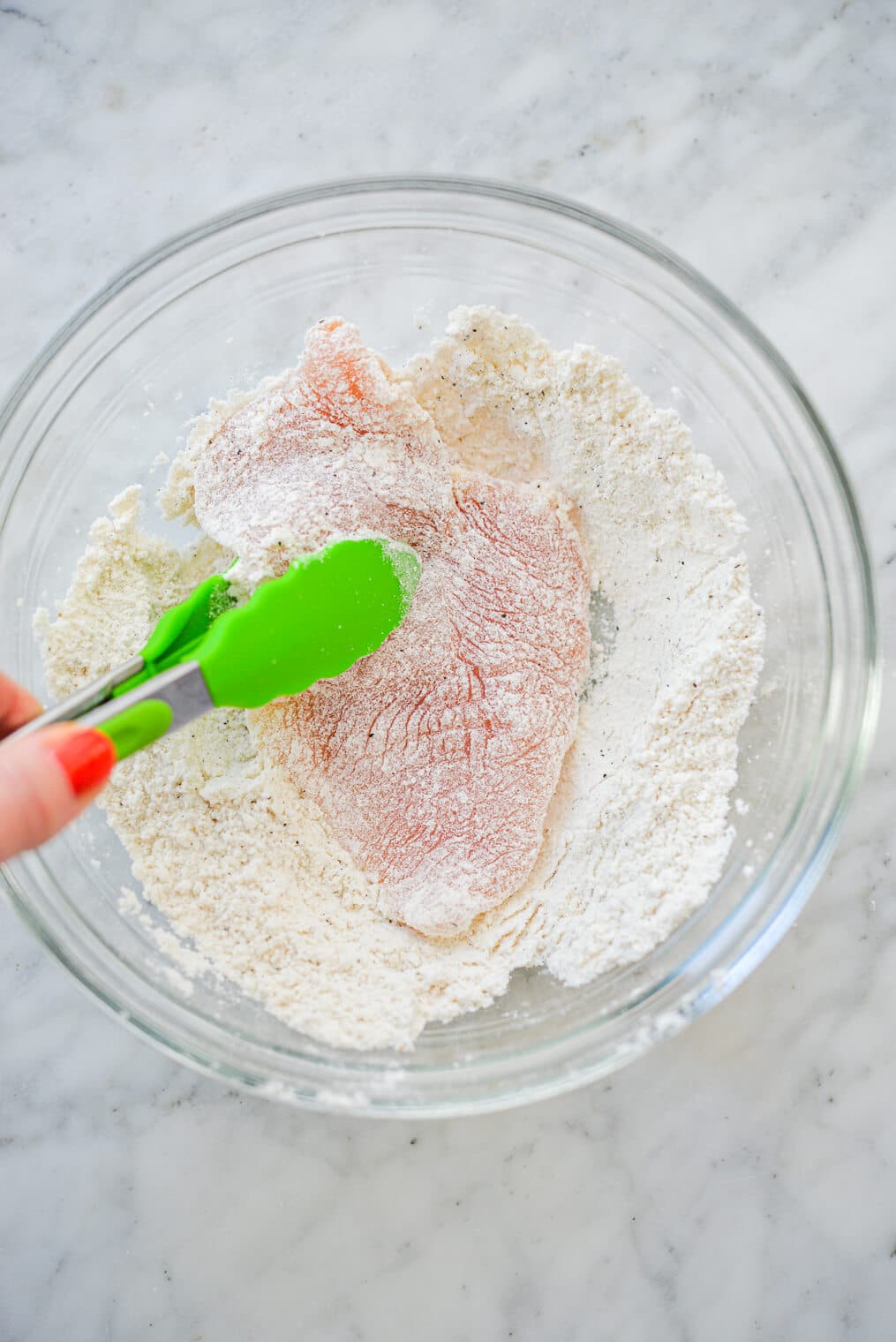 a person using tongs to coat chicken breasts in a flour mixture