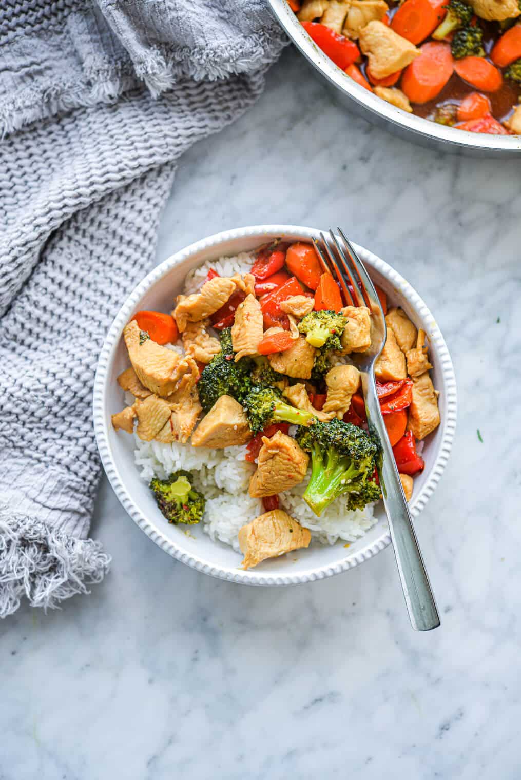 a serving of chicken stir fry in front of a skillet of chicken stir fry