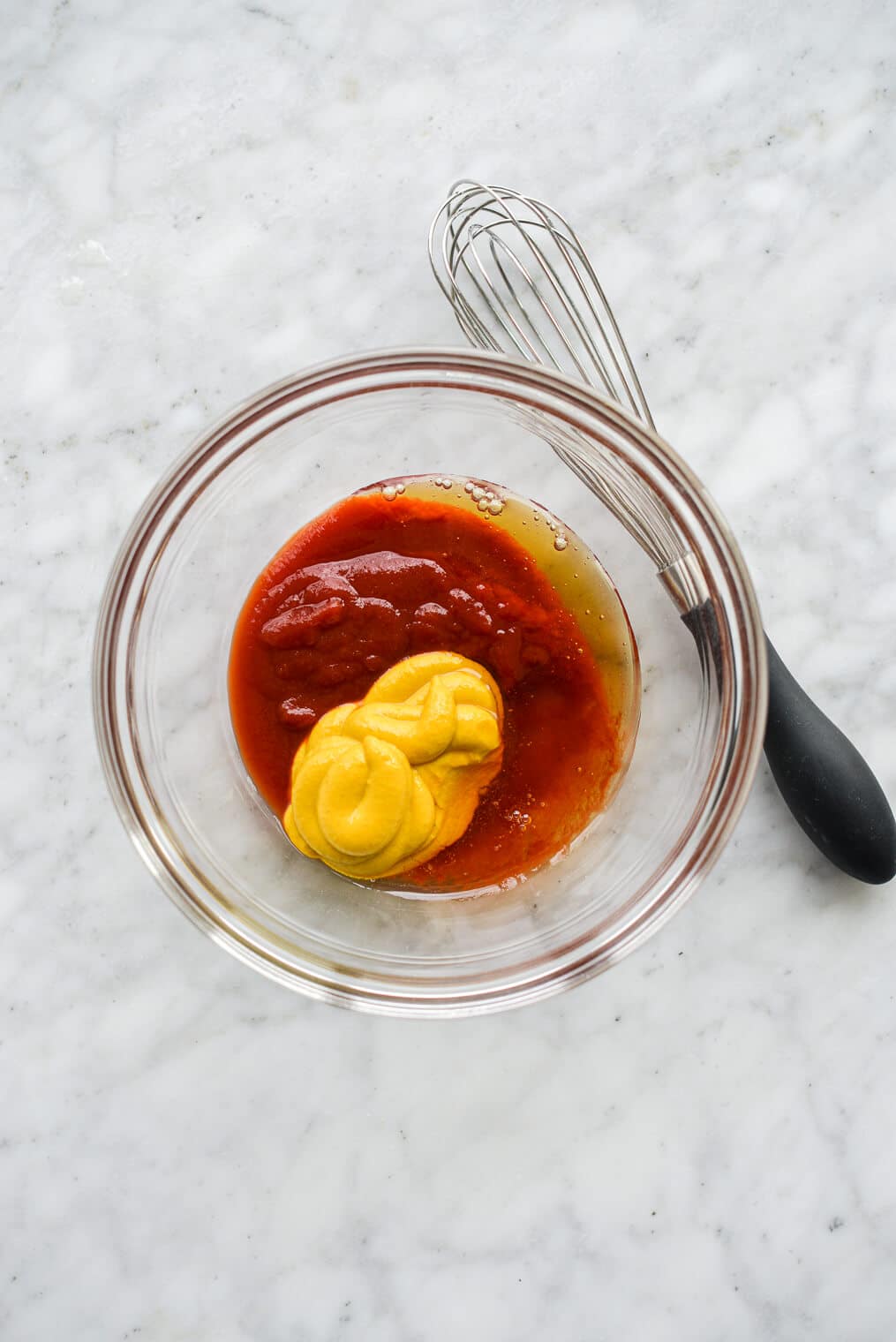 honey, mustard, and ketchup in a glass bowl next to a whisk