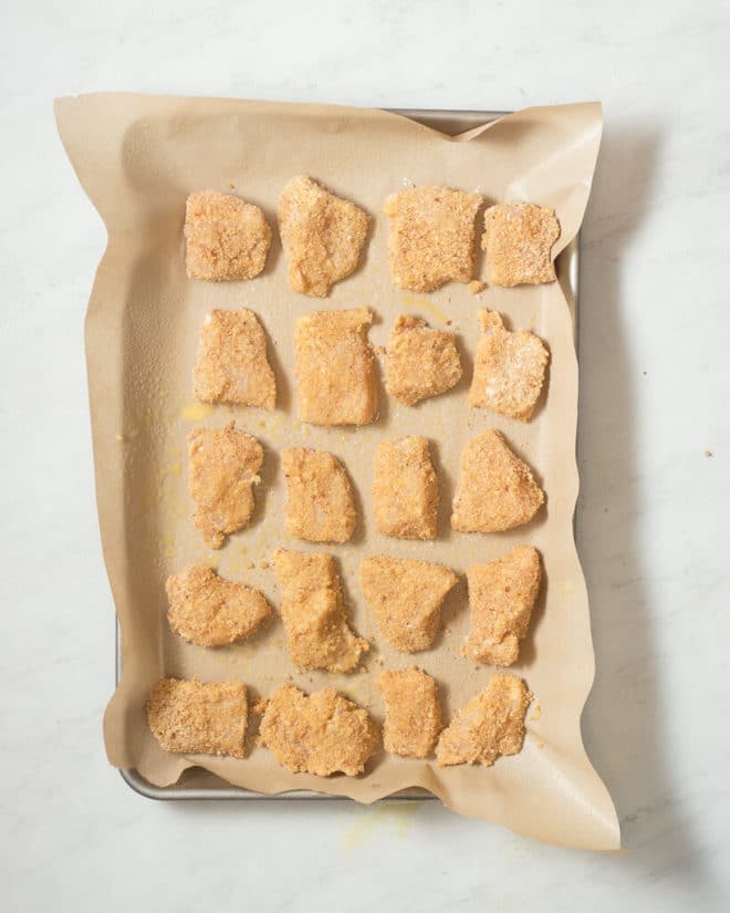 a baking sheet lined with parchment paper with raw chicken nuggets arranged on it in rows