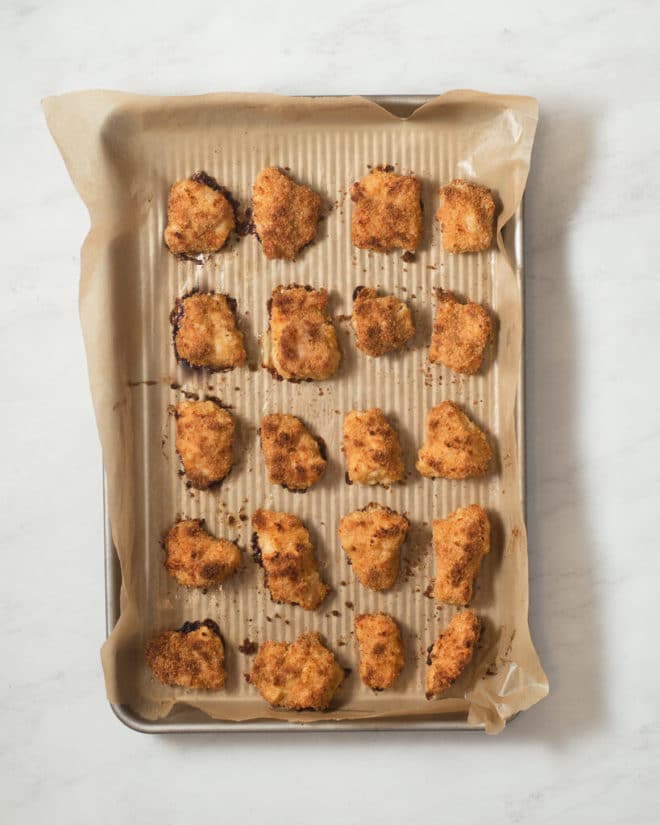a baking sheet lined with parchment paper with baked chicken nuggets arranged on it in rows