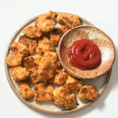 a plate of oven baked chicken nuggets next to a small bowl of red dipping sauce