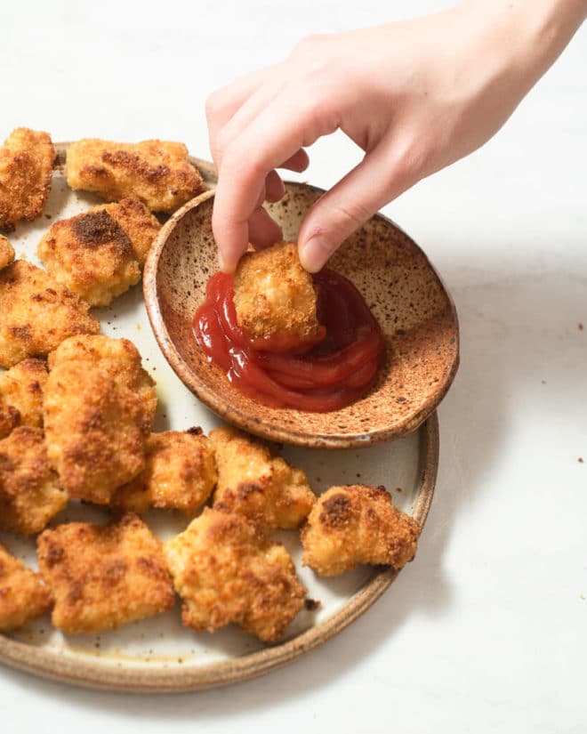 a person dipping an oven baked chicken nugget into a red dipping sauce